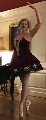 Me wearing a burgundy tutu and standing by a piano on pointe