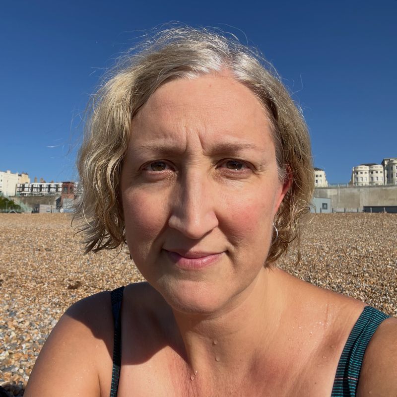 A selfie of me on the beach in a bathing suit squinting into the sun.