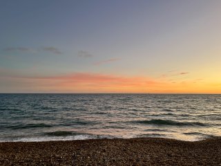 The bouncy sea and shingle shore under the evening sky with tangerine clouds on the horizon.