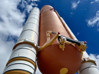 The space shuttle solid rocket boosters on display outside at Kennedy Space Center, white and orange against a deep blue sky,