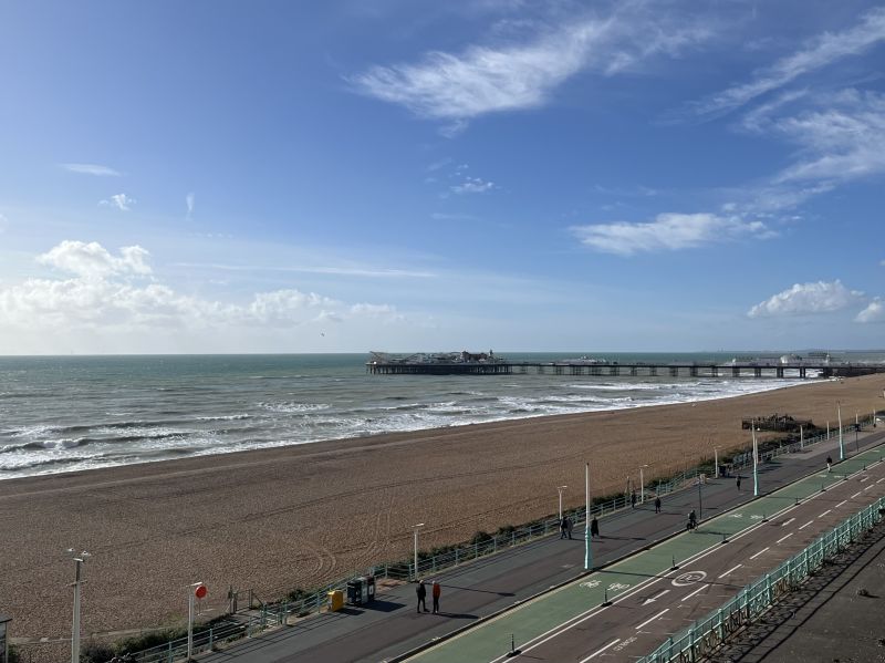 A long shot of Brighton Pier and the beach under a blue sky. It’s quite blustery and the sea is wavy and foamy.